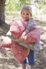 Портрет улыбающейся маленькой девочки, несущей подушки на улицу — стоковое фото