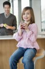 Girl drinking juice with father standing on background in kitchen — Stock Photo