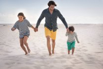 Glücklicher Vater läuft mit seinen Kindern am Strand — Stockfoto