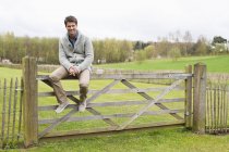 Человек, сидящий на деревянном заборе в поле — стоковое фото