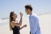 Женщина брызгает солнцезащитный крем на лицо мужа на пляже — стоковое фото