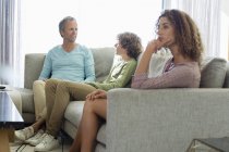 Bored woman sitting on sofa in living room with husband and son on background — Stock Photo