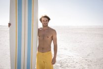 Happy young man holding surfboard on beach — Stock Photo