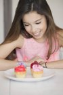 Chica sonriente mirando cupcakes en la mesa - foto de stock