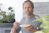 Porträt eines reifen Mannes, der Obstsalat in der Küche isst — Stockfoto