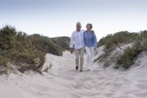 Feliz casal sênior andando na praia de areia ao pôr do sol — Fotografia de Stock