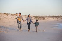 Famille marchant sur la plage de sable tenant la main au coucher du soleil — Photo de stock