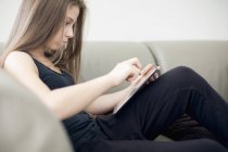 Adolescente utilisant une tablette numérique sur le canapé à la maison — Photo de stock