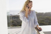 Femme blonde adulte moyenne parlant sur un téléphone portable sur un balcon dans la nature — Photo de stock