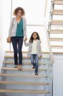 Счастливые мать и дочь держатся за руки на лестнице в здании — стоковое фото