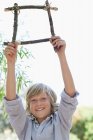 Porträt eines niedlichen Jungen mit einem Rahmen aus Treibholz und erhobenen Armen im Freien — Stockfoto