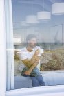 Jeune homme regardant par la fenêtre avec une tasse de café — Photo de stock