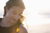 Sonriente joven mujer de pie en la playa a la luz del sol - foto de stock