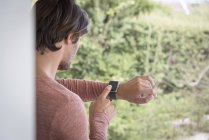 Junger Mann kontrolliert Zeit mit Smartwatch im Garten — Stockfoto