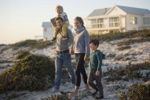 Paar mit Kindern spazieren am Strand mit Haus im Hintergrund — Stockfoto
