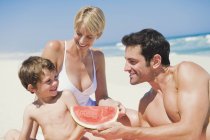 Family enjoying watermelon on sandy beach — Stock Photo