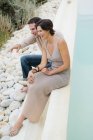 Couple riant assis au bord de la piscine et vue admirative — Photo de stock