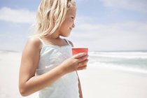 Маленька дівчинка тримає одноразову чашку на пляжі і дивиться на погляд — стокове фото