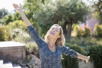 Щаслива жінка з простягнутими руками стоїть в саду — стокове фото