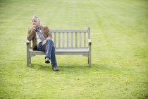 Вдумливий чоловік сидить на дерев'яній лавці в зеленому полі — стокове фото