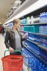 Femme souriante achetant une bouteille d'eau en magasin — Photo de stock