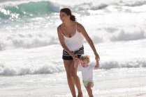 Mãe feliz com seu filhinho andando na praia — Fotografia de Stock