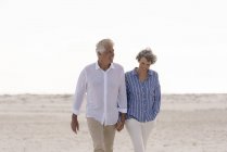 Heureux couple de personnes âgées marchant sur la plage se tenant la main — Photo de stock