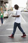 Young man text messaging with mobile phone while crossing road — Stock Photo