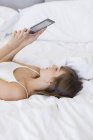 Молода жінка лежить на ліжку і читає електронну книгу — стокове фото