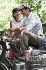 Sonriente pareja sentada en bicicletas y hablando en la ciudad - foto de stock