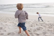 Вид ззаду хлопчика, що біжить на пляжі зі своєю сестрою — стокове фото