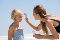Beautiful woman applying sunscreen on her daughter face — Stock Photo