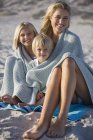Portrait d'une mère et d'enfants souriants enveloppés dans un châle assis sur la plage — Photo de stock