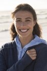 Portrait of charming young woman in warm hoodie smiling on beach — Stock Photo