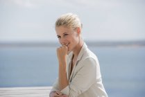 Young smiling woman sitting at table on lake shore — Stock Photo