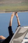 Mujer tomando selfie con el teléfono móvil en la silla de cubierta en el paseo marítimo - foto de stock