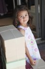 Portrait of cute little girl standing at stack of boxes — Stock Photo