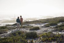 Романтическая пара, стоящая на берегу моря и смотрящая на вид — стоковое фото