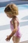 Nahaufnahme eines kleinen Mädchens in rosa Badebekleidung, das in der Nähe eines Swimmingpools spaziert — Stockfoto