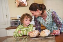 Mignon petit garçon et mère cuisson du pain dans la cuisine — Photo de stock