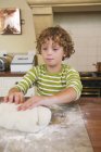 Mignon petit garçon pétrissant la pâte dans la cuisine — Photo de stock