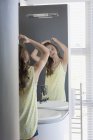 Teenage girl examining hair in mirror — Stock Photo