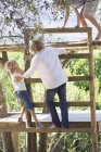 Children climbing ladders to tree house in garden — Stock Photo