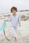 Мальчик держит флаг на палочке и ходит по песчаному пляжу — стоковое фото