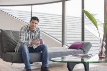 Mann sitzt mit Tasse Kaffee auf Couch und blickt in Kamera — Stockfoto