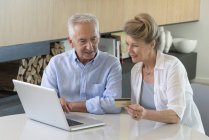 Senior pareja de compras en línea con el ordenador portátil en casa - foto de stock