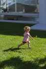 Cute baby girl playing on grass in front of building — Stock Photo