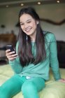 Портрет улыбающейся девушки с помощью мобильного телефона на кровати — стоковое фото
