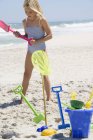 Ragazza in costume da bagno in piedi con giocattoli sulla spiaggia di sabbia — Foto stock