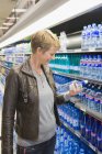Усміхнена жінка купує пляшку води в магазині — стокове фото